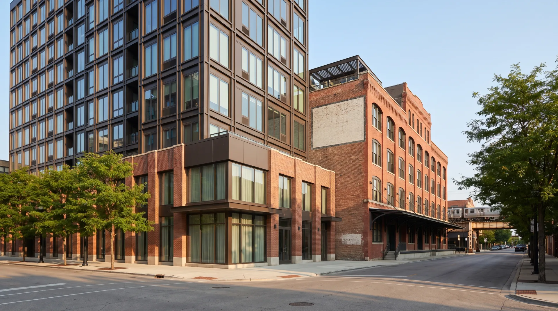 A new eleven-story bronze and brick apartment building on a West Loop corner beside a red-brick former warehouse, with the elevated train at the end of the street.
