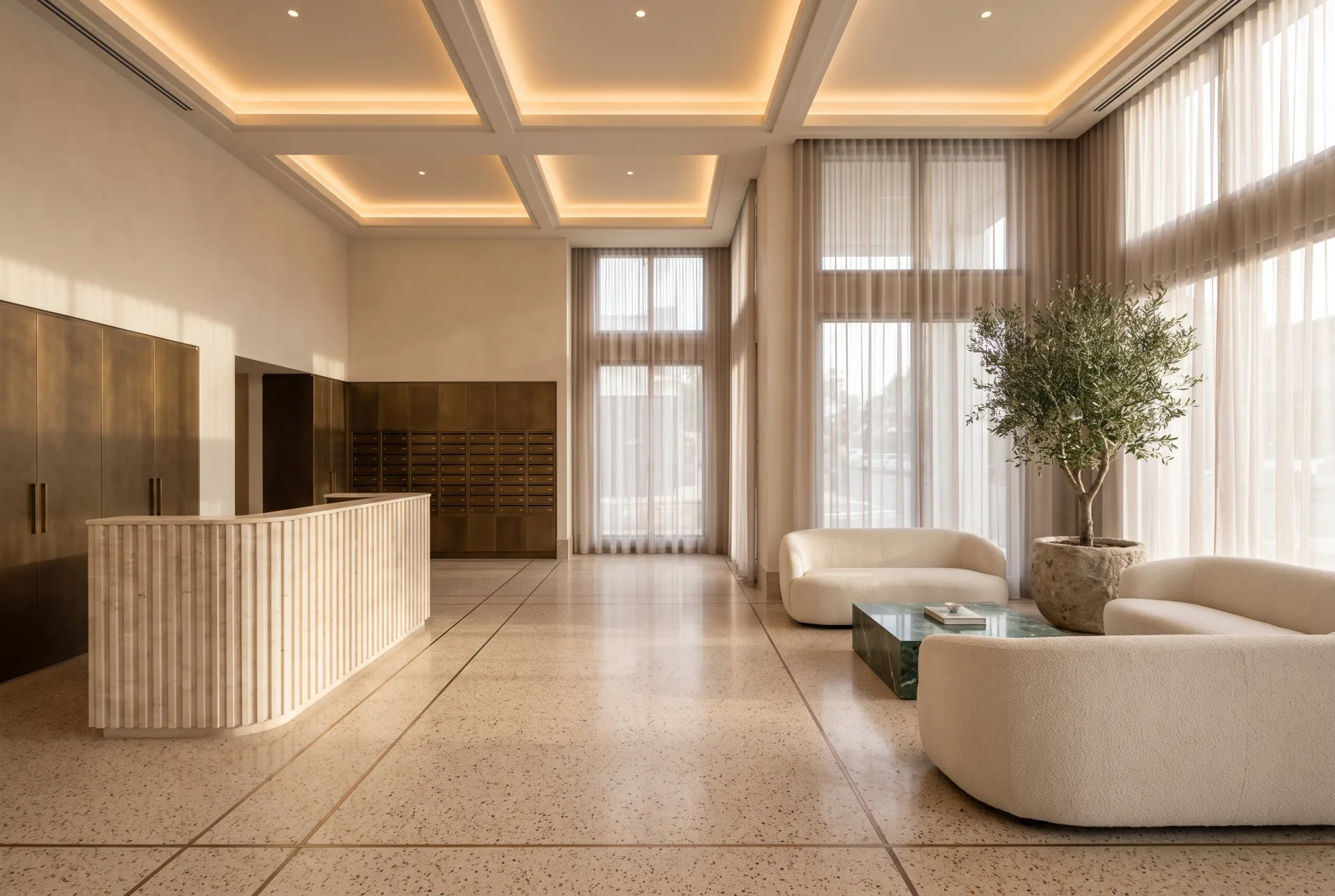 A double-height apartment lobby with a fluted travertine desk, bronze mail lockers, curved sofas and an olive tree.