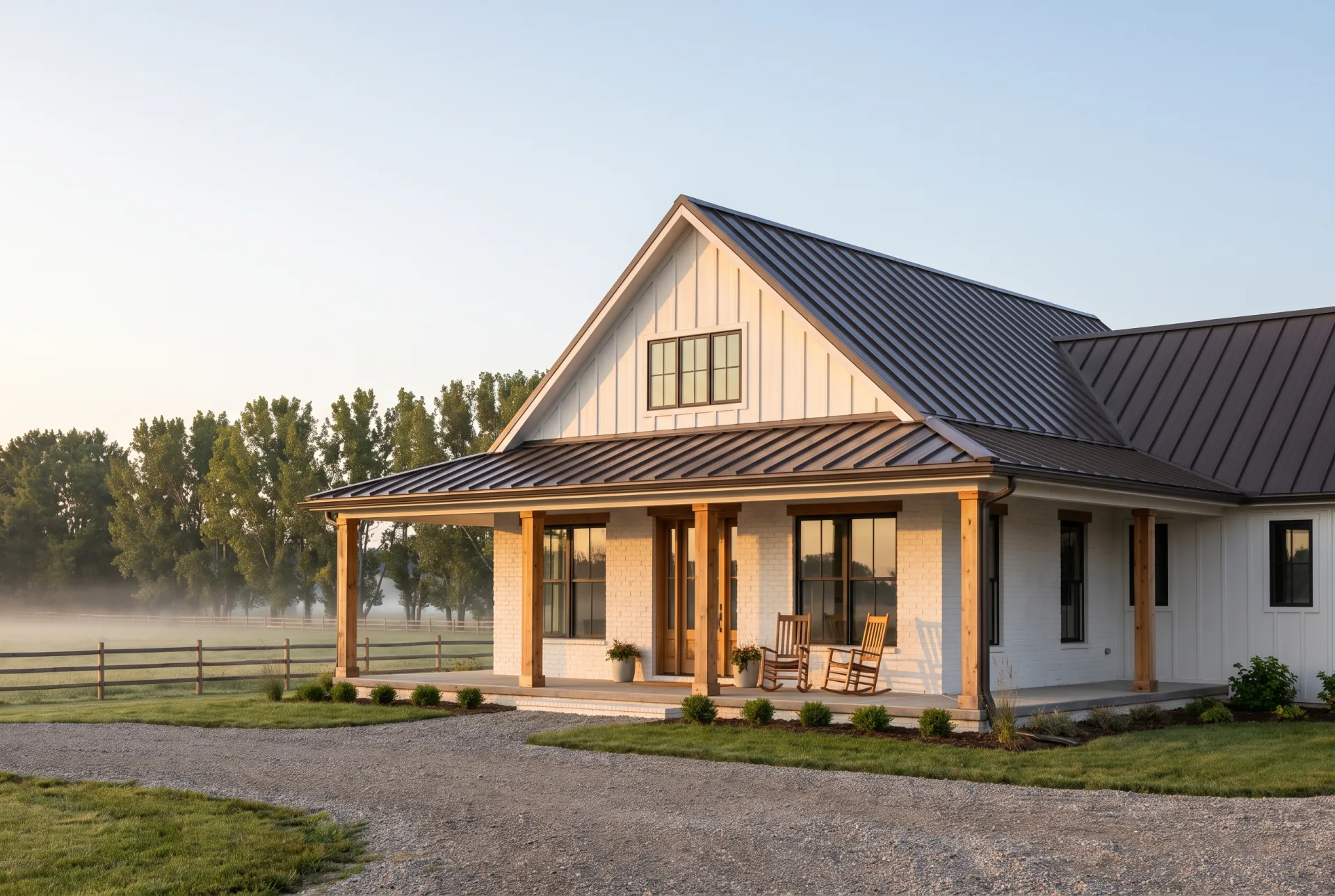 A single-story limewashed brick farmhouse with a bronze metal roof and wraparound cedar porch beside a misty pasture.