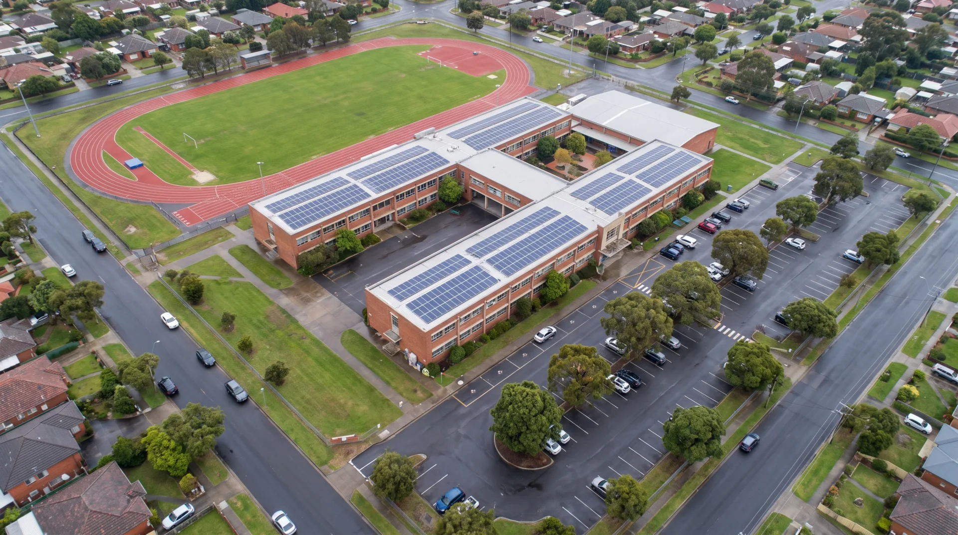 Concept work: a school campus from above with three wings around a courtyard, a running track, sports field and solar panels on the roofs.